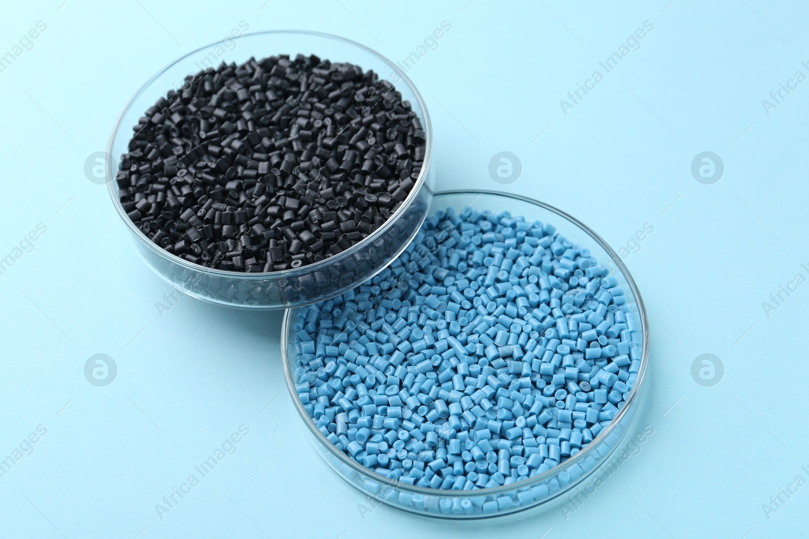 Photo of Colorful plastic granules in petri dishes on light blue background