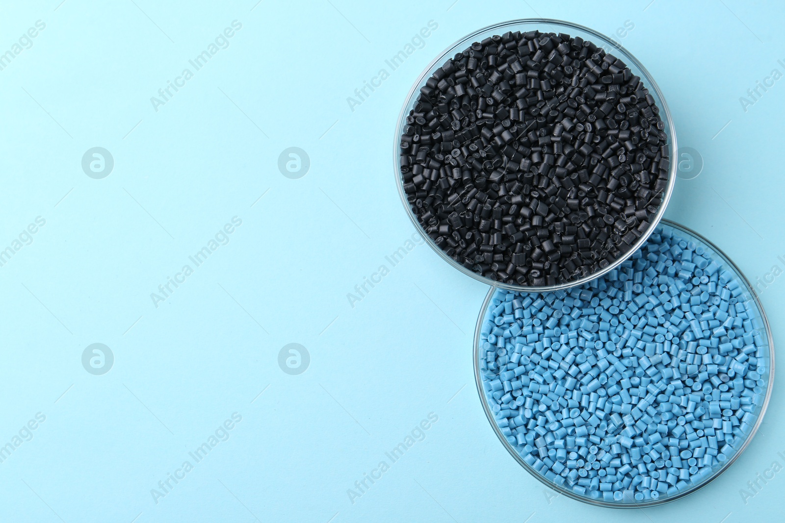 Photo of Colorful plastic granules in petri dishes on light blue background, top view. Space for text