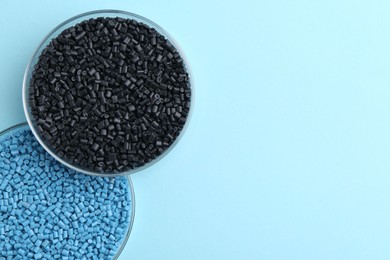 Photo of Colorful plastic granules in petri dishes on light blue background, top view. Space for text