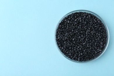 Photo of Black plastic granules in petri dish on light blue background, top view. Space for text