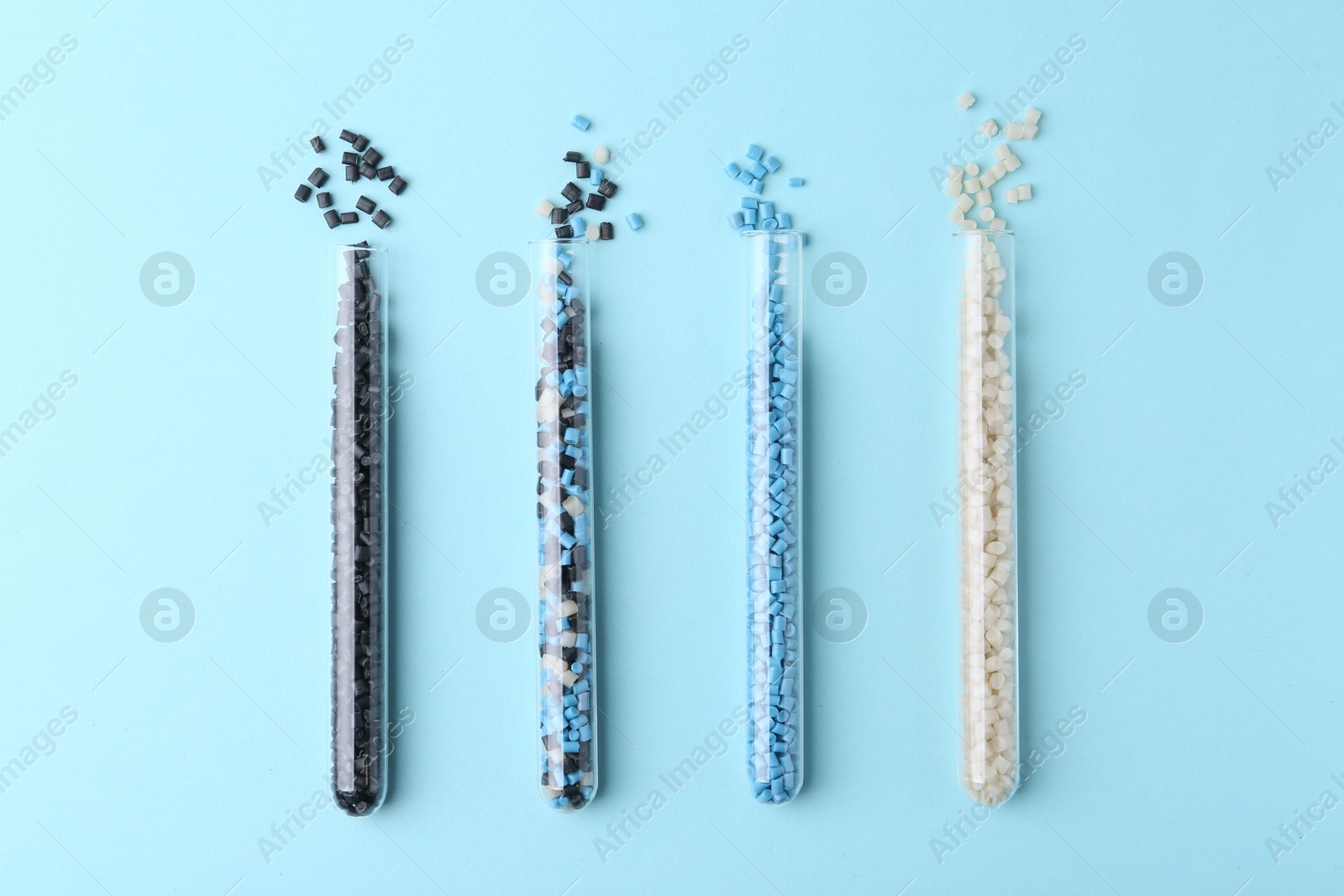 Photo of Colorful plastic granules in test tubes on light blue background, flat lay