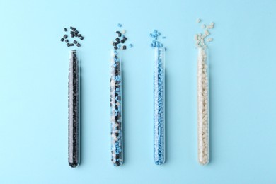 Colorful plastic granules in test tubes on light blue background, flat lay