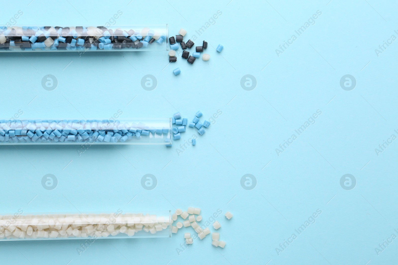 Photo of Colorful plastic granules in test tubes on light blue background, flat lay. Space for text