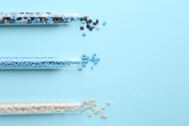 Photo of Colorful plastic granules in test tubes on light blue background, flat lay. Space for text