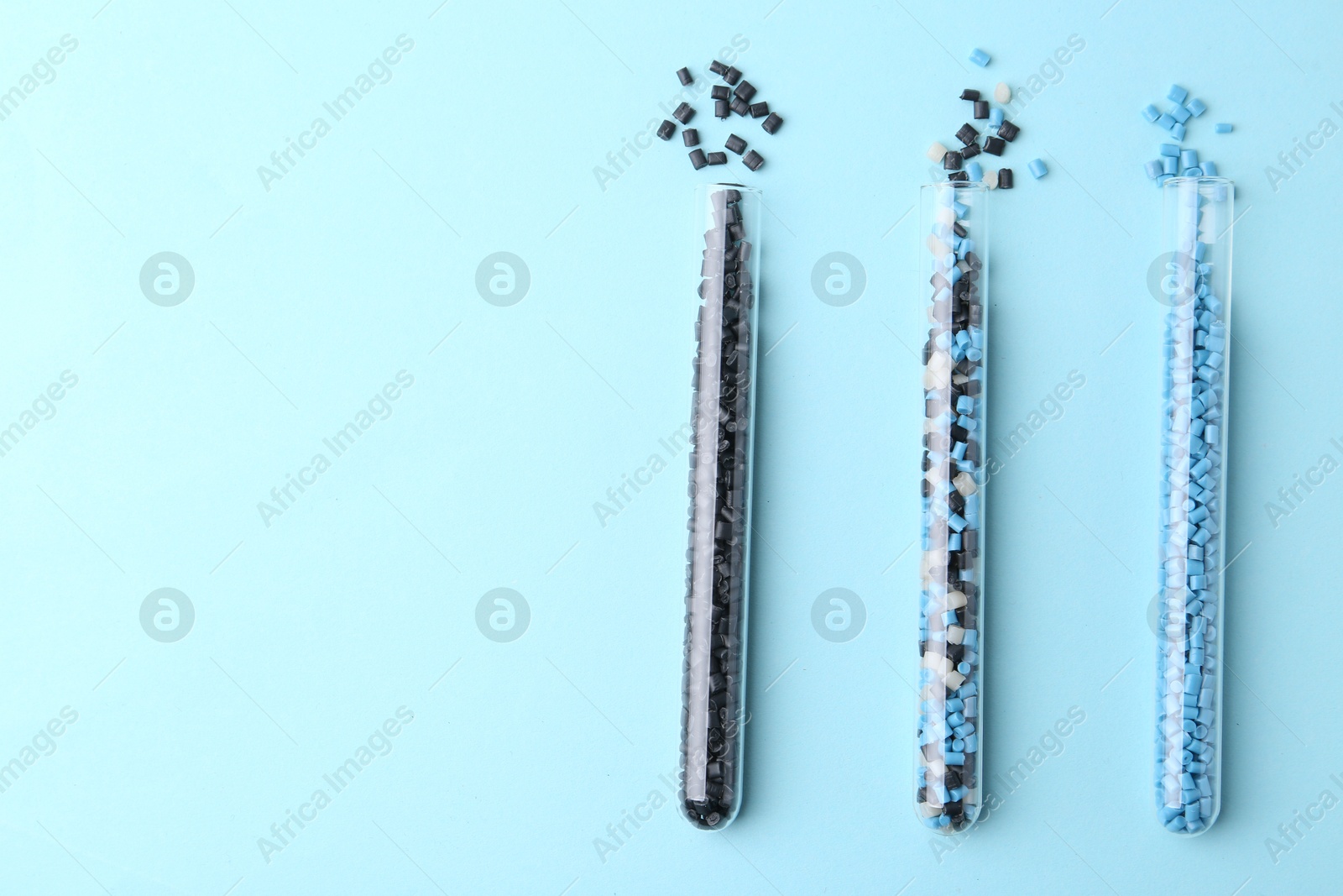 Photo of Colorful plastic granules in test tubes on light blue background, flat lay. Space for text