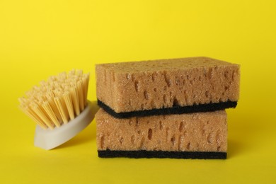 Photo of Sponges and cleaning brush on yellow background, closeup