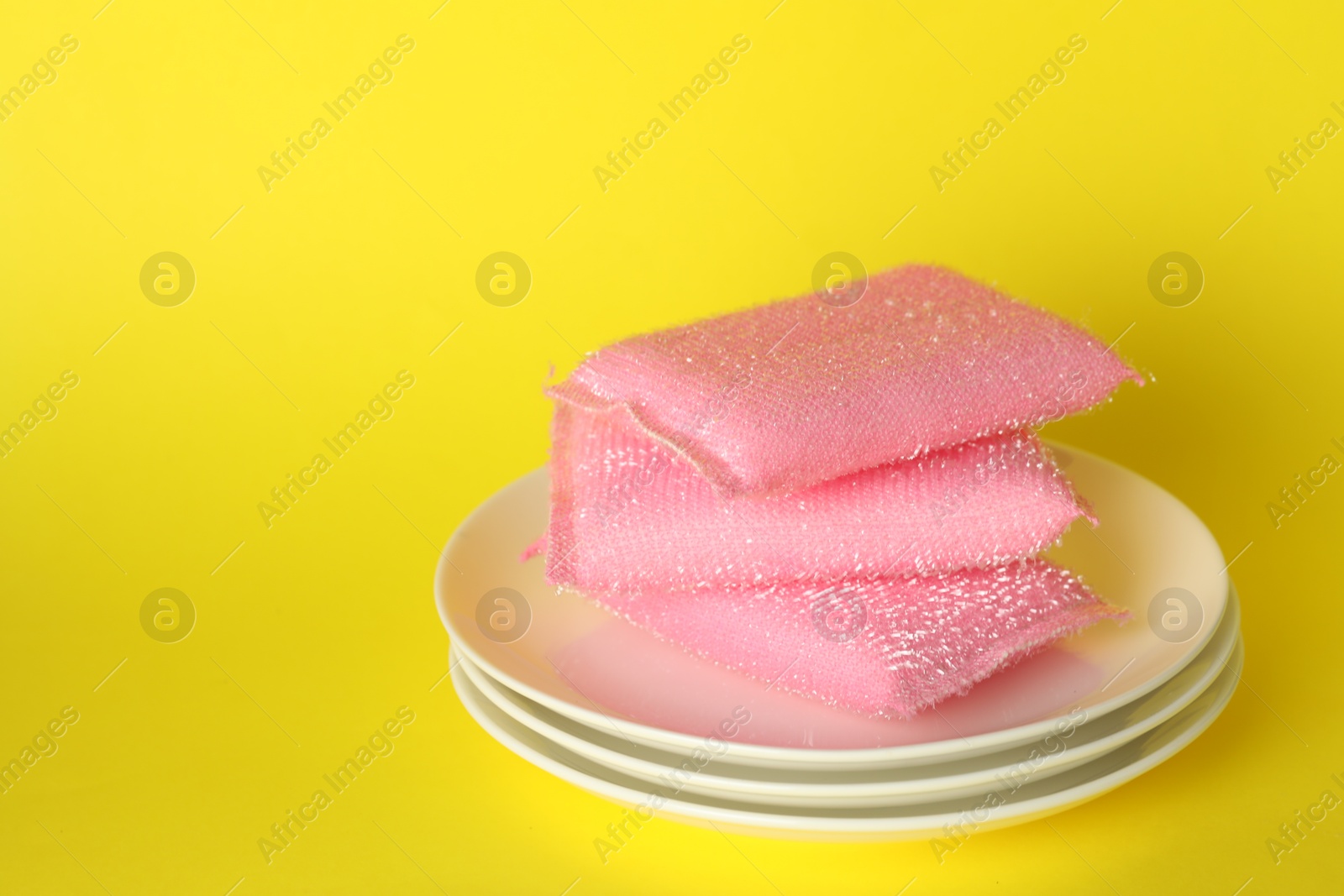 Photo of Stack of sponges and plates on yellow background, closeup. Space for text