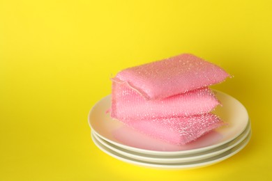 Photo of Stack of sponges and plates on yellow background, closeup. Space for text