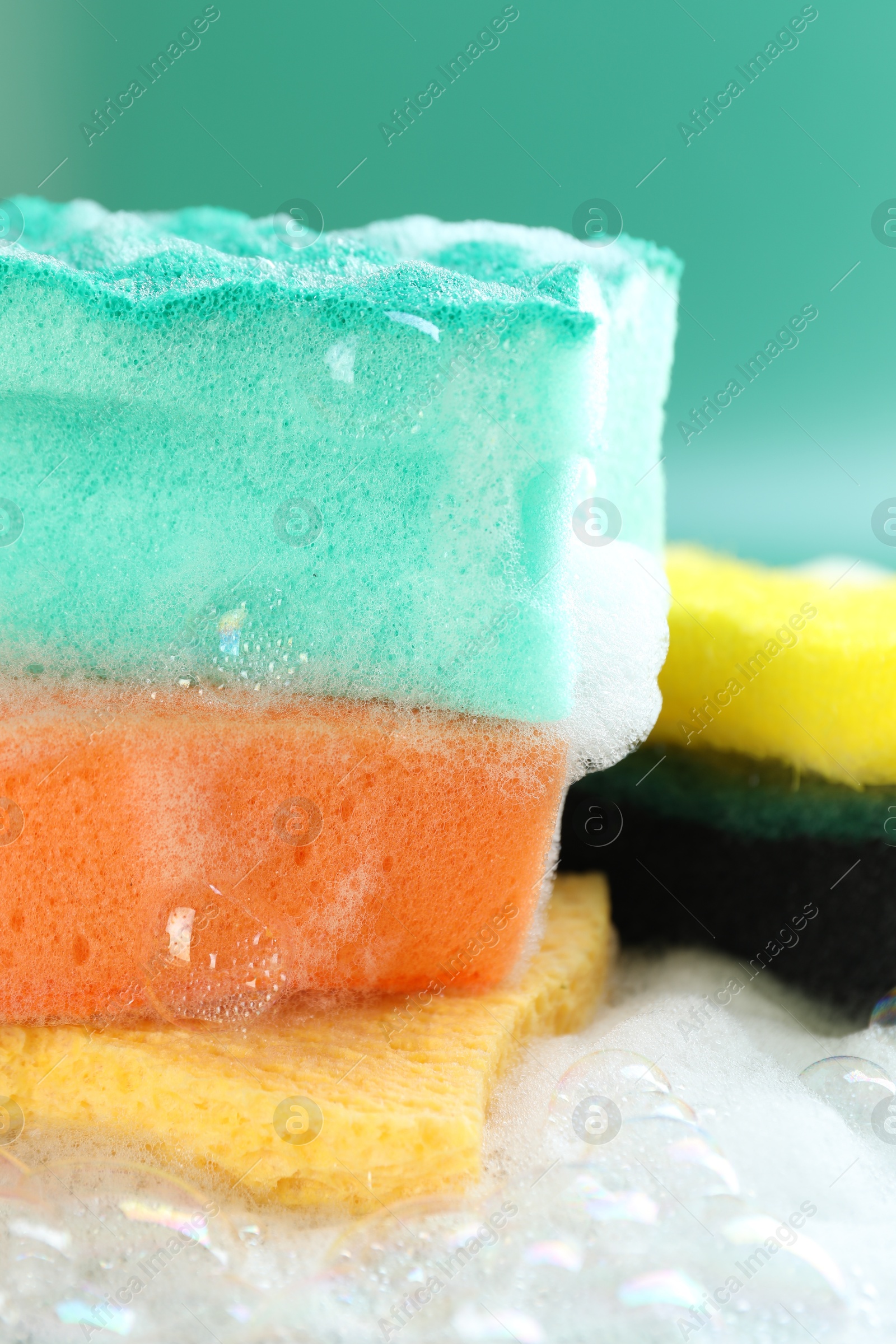 Photo of Different clean sponges with foam on green background, closeup