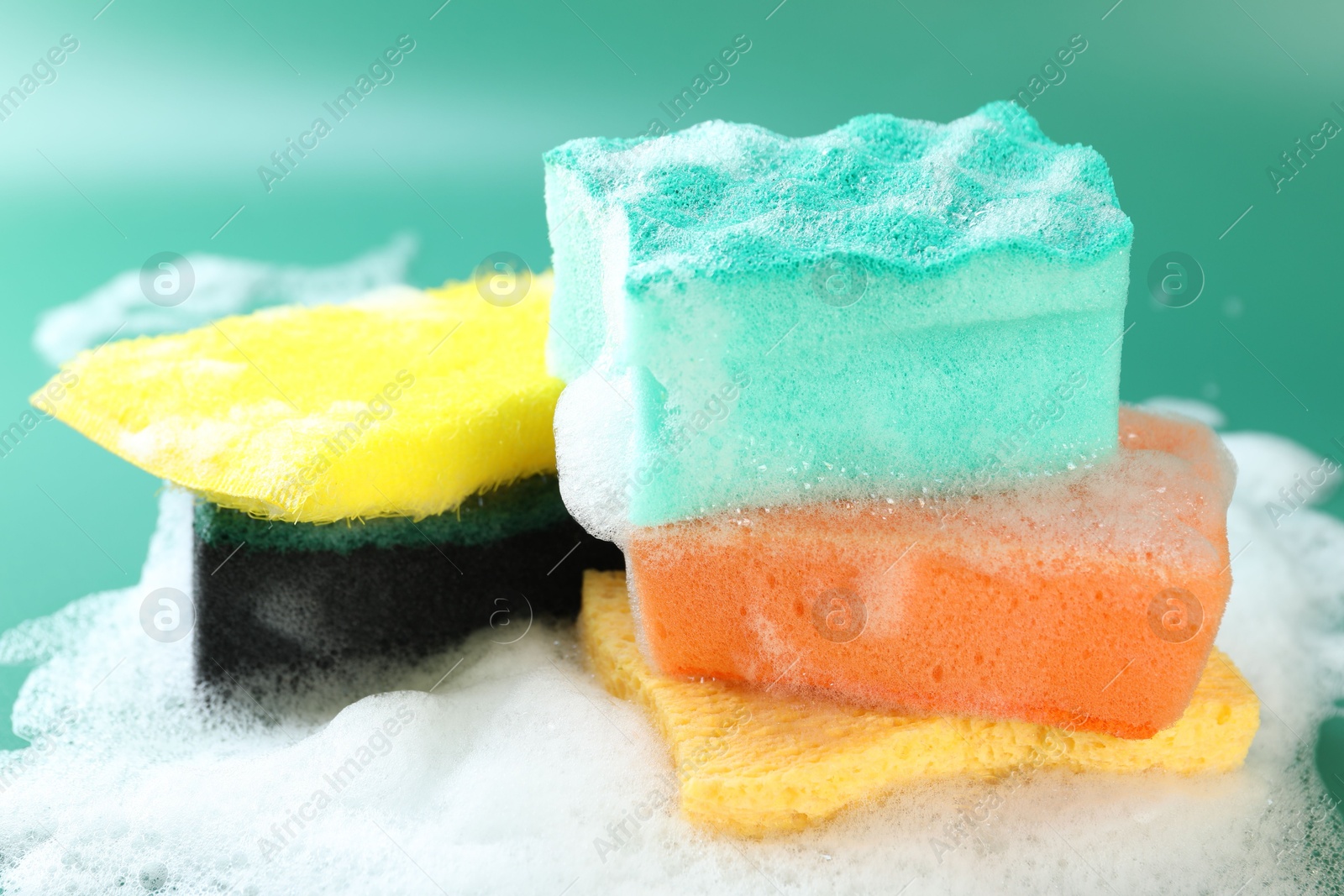 Photo of Different clean sponges with foam on green background, closeup