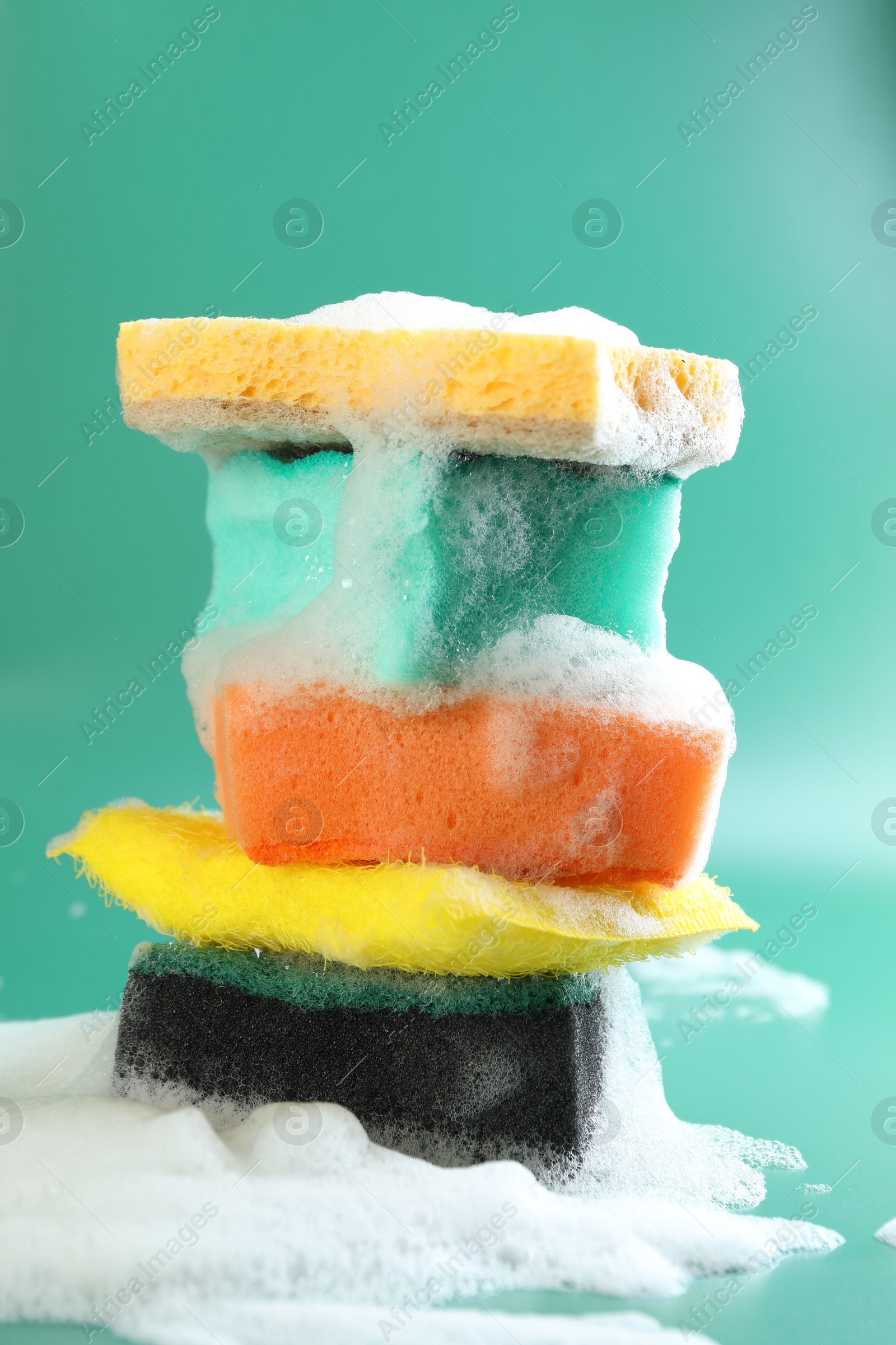 Photo of Stack of different clean sponges with foam on green background, closeup