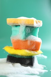 Photo of Stack of different clean sponges with foam on green background, closeup