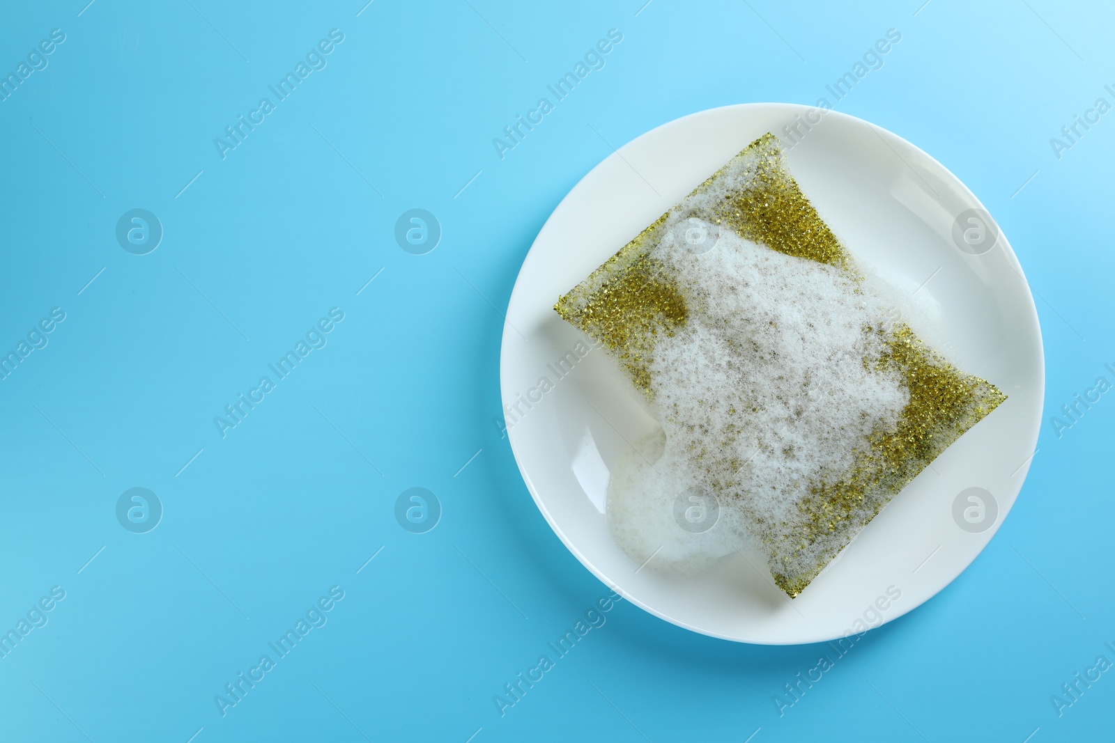 Photo of One sponge with foam and plate on light blue background, top view. Space for text