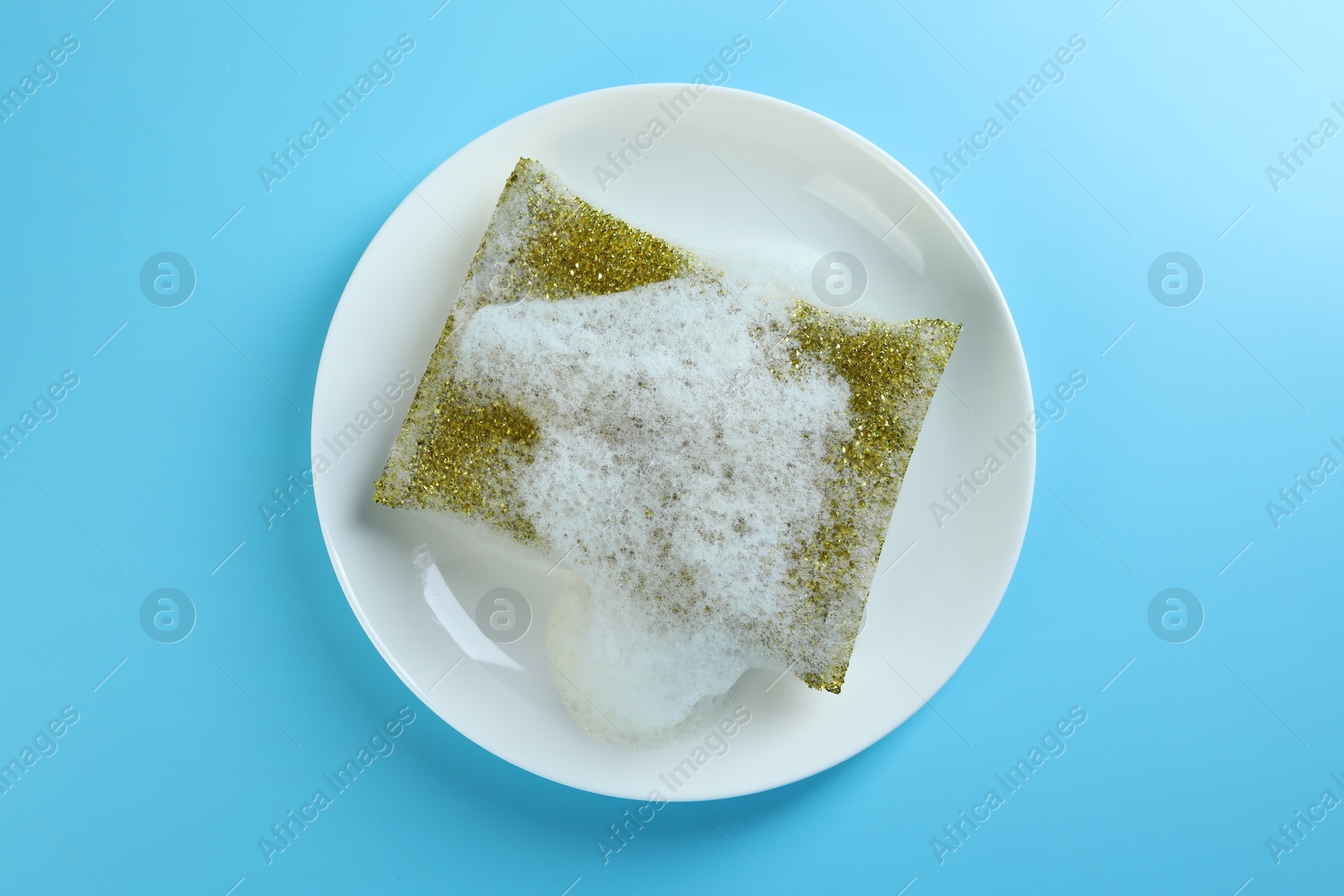 Photo of One sponge with foam and plate on light blue background, top view