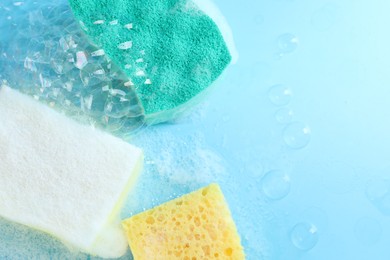 Photo of Colorful sponges with foam and bubbles on light blue background, flat lay. Space for text