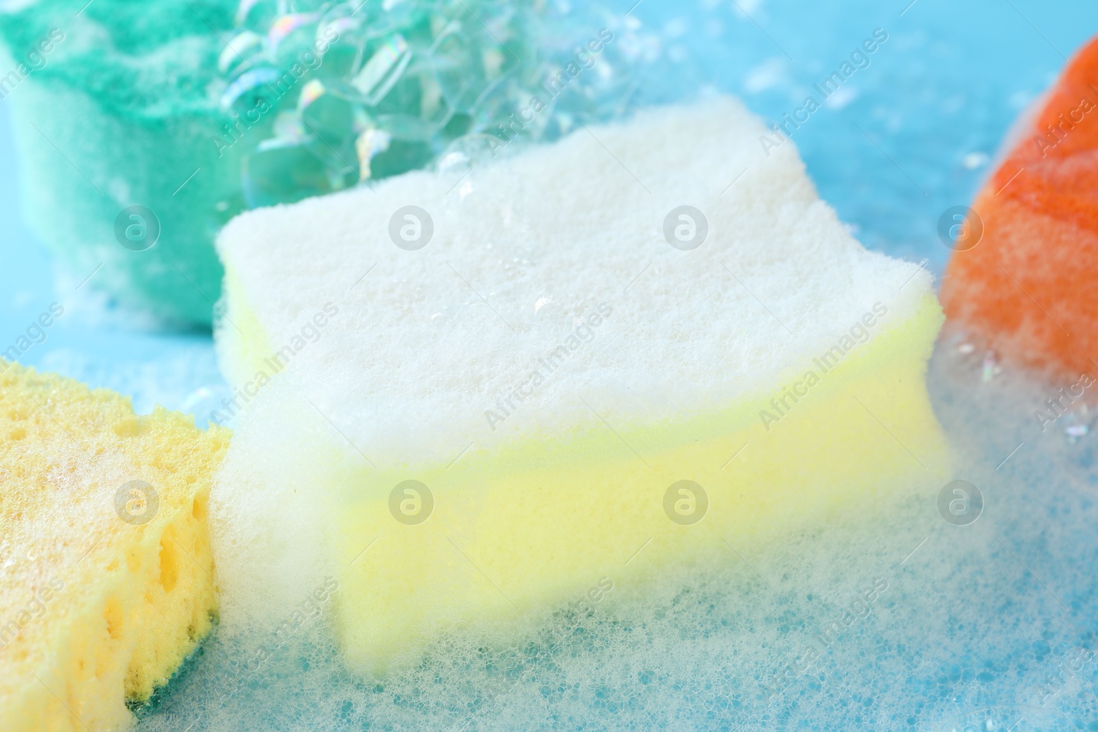 Photo of Colorful sponges with foam and bubbles on light blue background, closeup