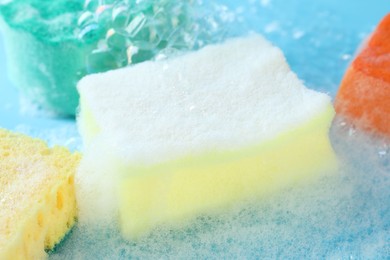 Photo of Colorful sponges with foam and bubbles on light blue background, closeup