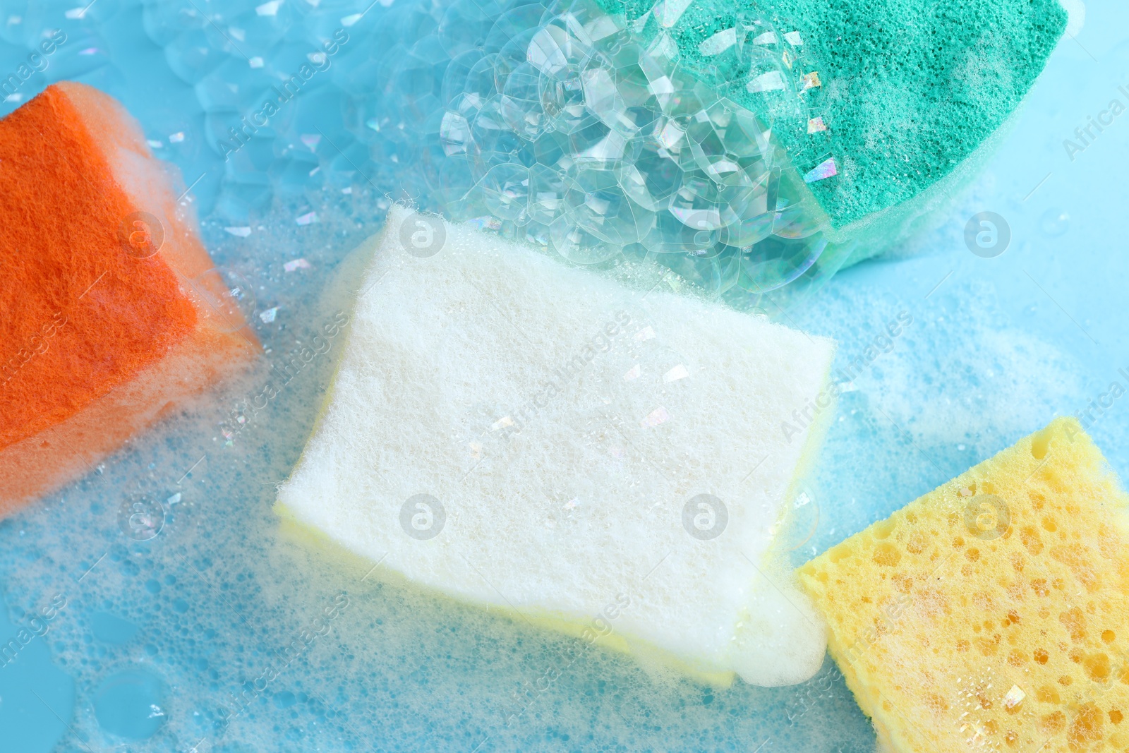 Photo of Colorful sponges with foam and bubbles on light blue background, flat lay