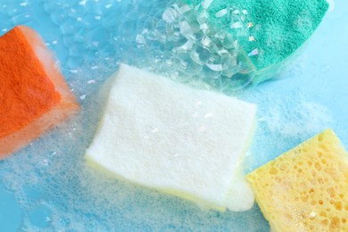 Photo of Colorful sponges with foam and bubbles on light blue background, flat lay