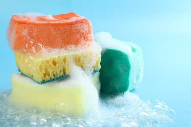 Photo of Colorful sponges with foam and bubbles on light blue background, closeup. Space for text