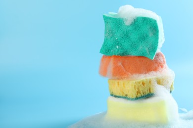 Photo of Stack of colorful sponges with foam on light blue background, closeup. Space for text