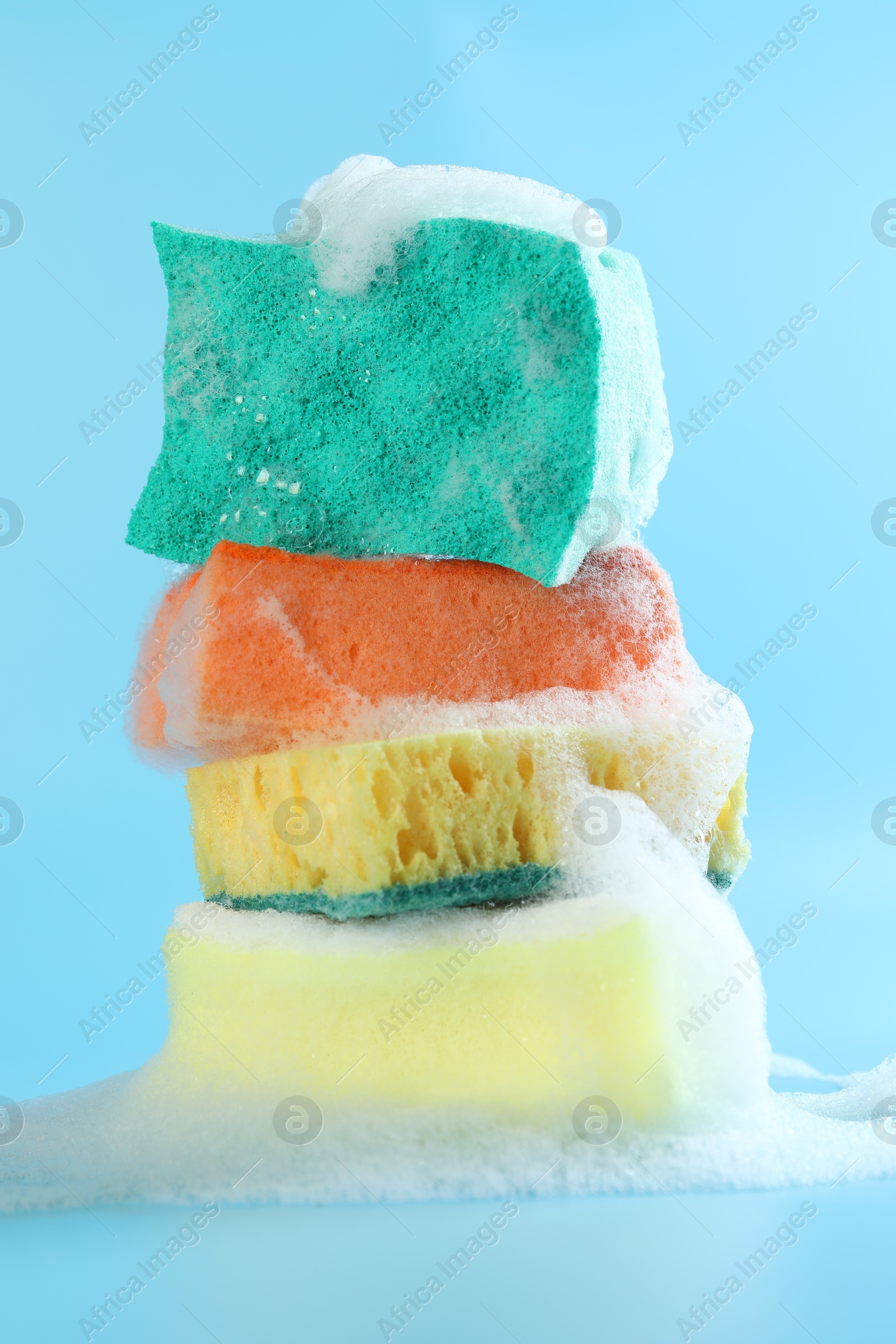 Photo of Stack of colorful sponges with foam on light blue background, closeup