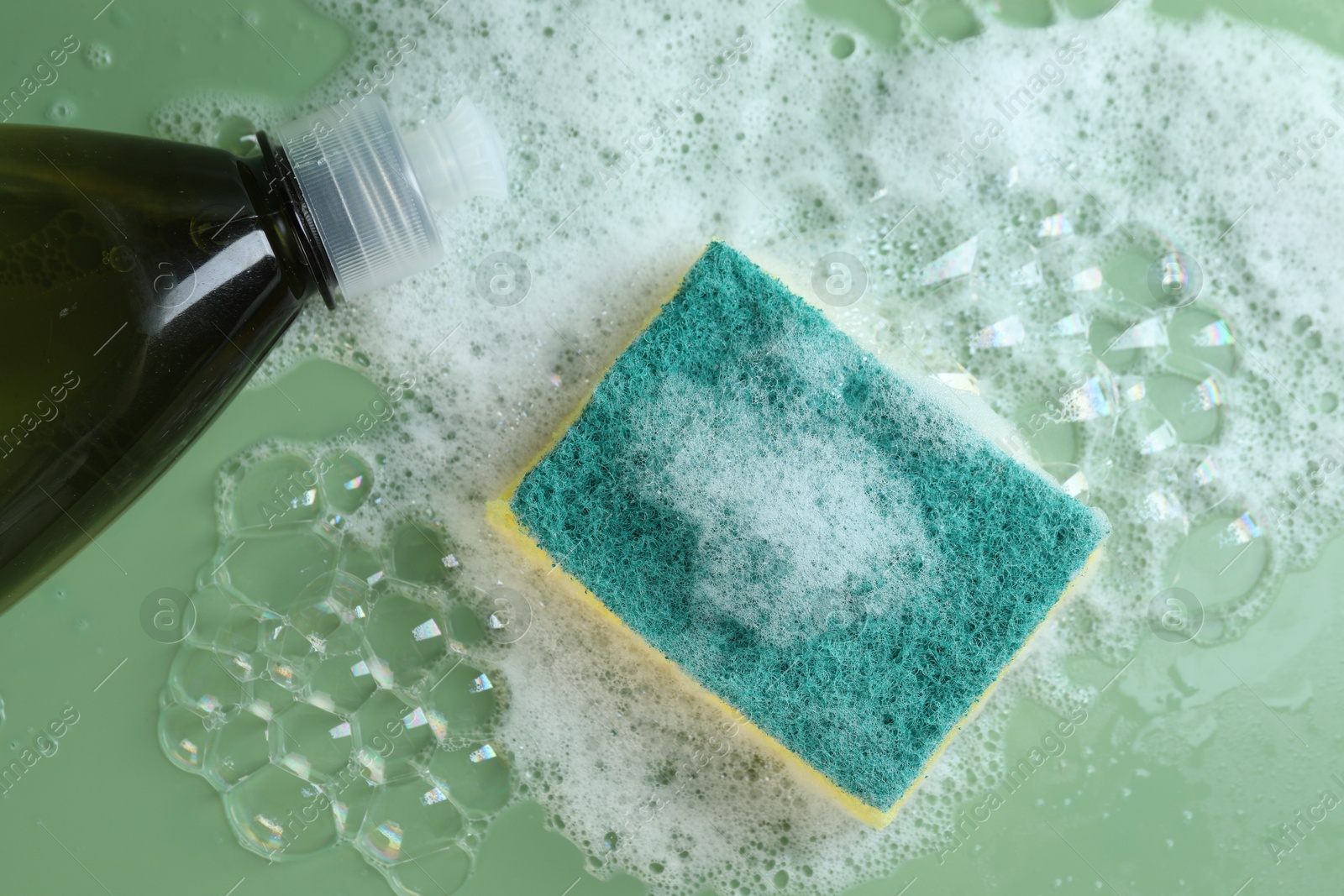 Photo of Sponge with foam, detergent and bubbles on green background, flat lay