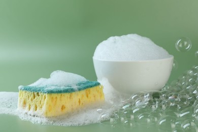 Photo of Sponge with foam, bowl and bubbles on green background, closeup