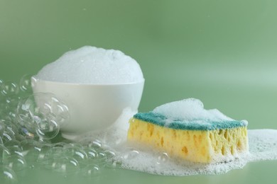 Photo of Sponge with foam, bowl and bubbles on green background, closeup