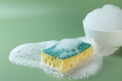 Photo of Sponge with foam, bowl and bubbles on green background, closeup