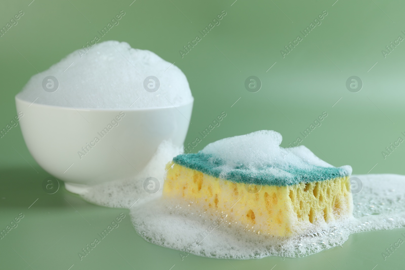 Photo of Sponge with foam, bowl and bubbles on green background, closeup