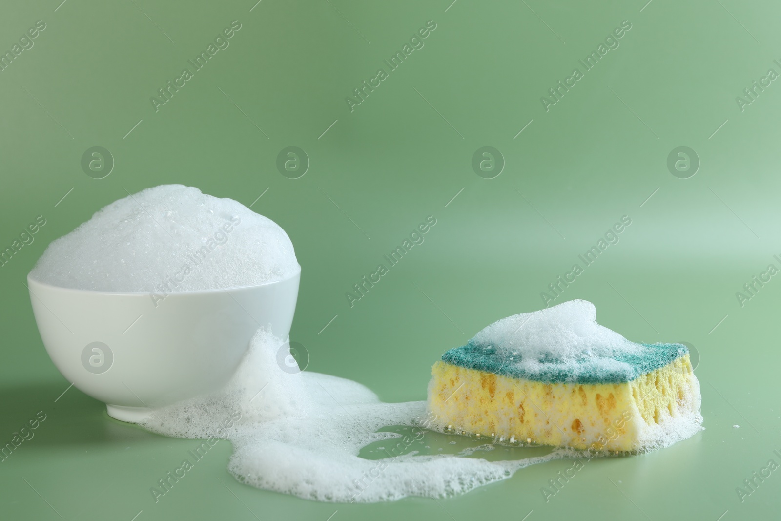 Photo of Sponge with foam, bowl and bubbles on green background, closeup