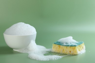 Photo of Sponge with foam, bowl and bubbles on green background, closeup