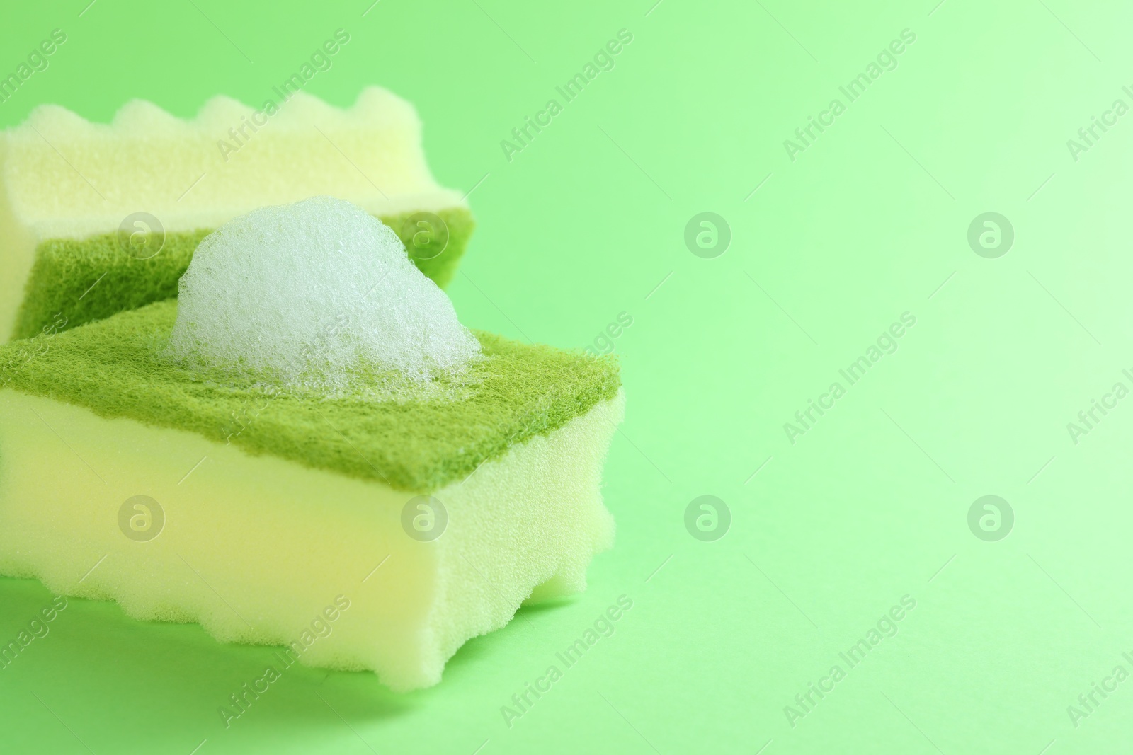 Photo of Sponges with foam on green background, closeup. Space for text