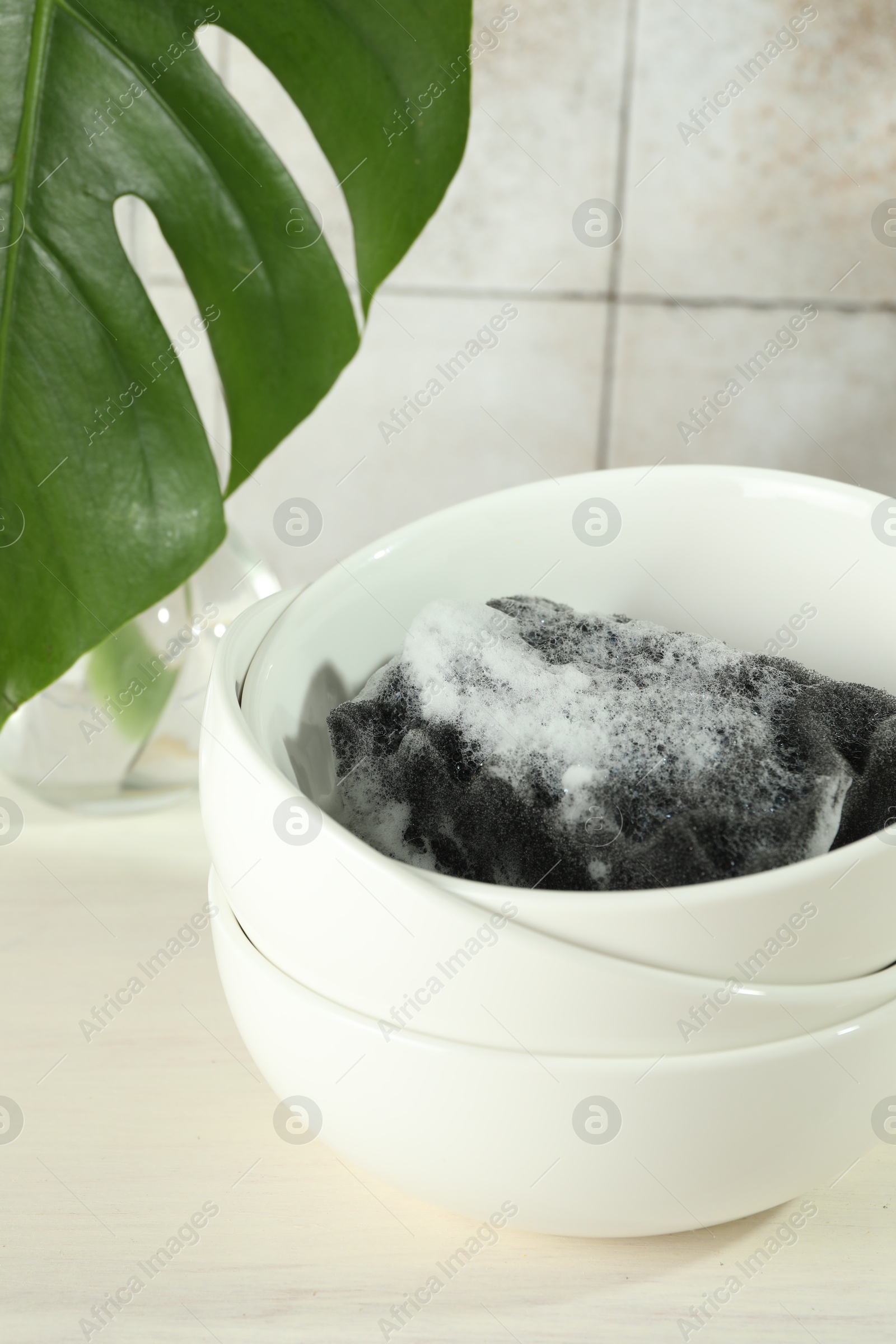 Photo of Sponge with foam and stack of bowls on light wooden table, closeup