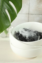 Photo of Sponge with foam and stack of bowls on light wooden table, closeup