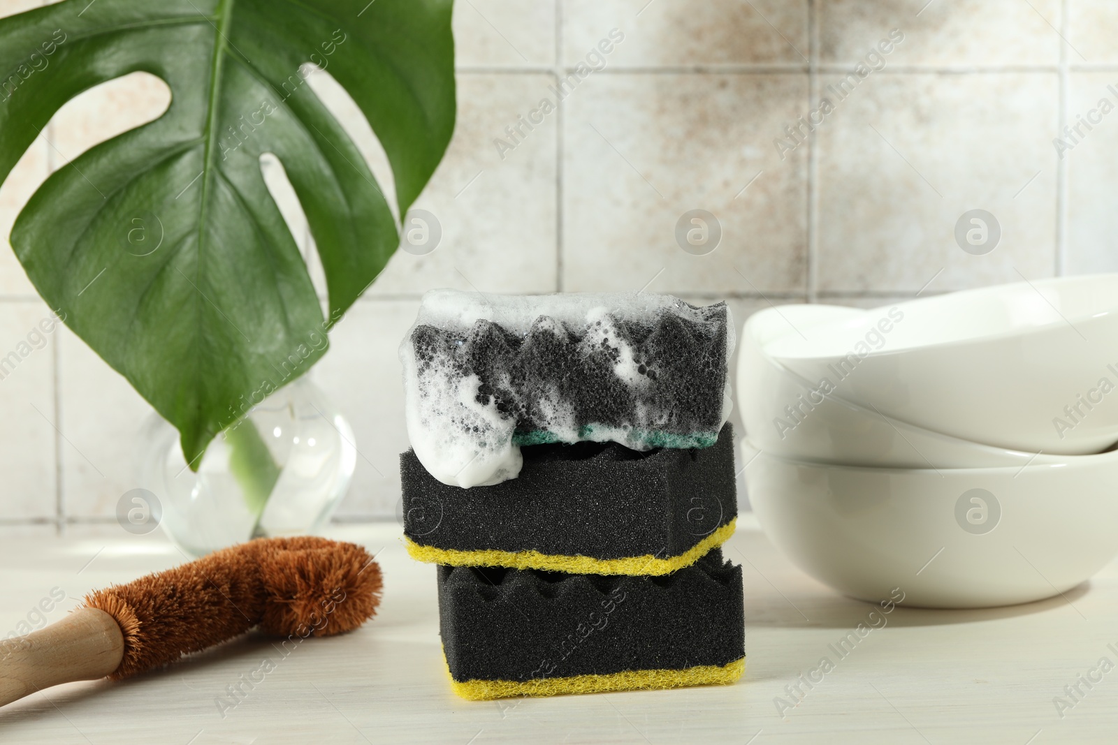 Photo of Sponge with foam, brush and stack of bowls on light wooden table, closeup