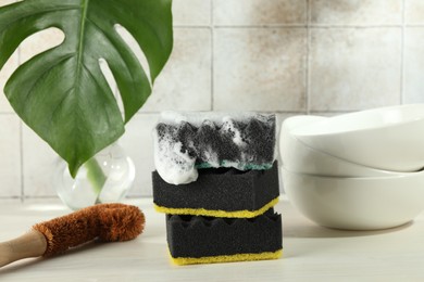 Photo of Sponge with foam, brush and stack of bowls on light wooden table, closeup