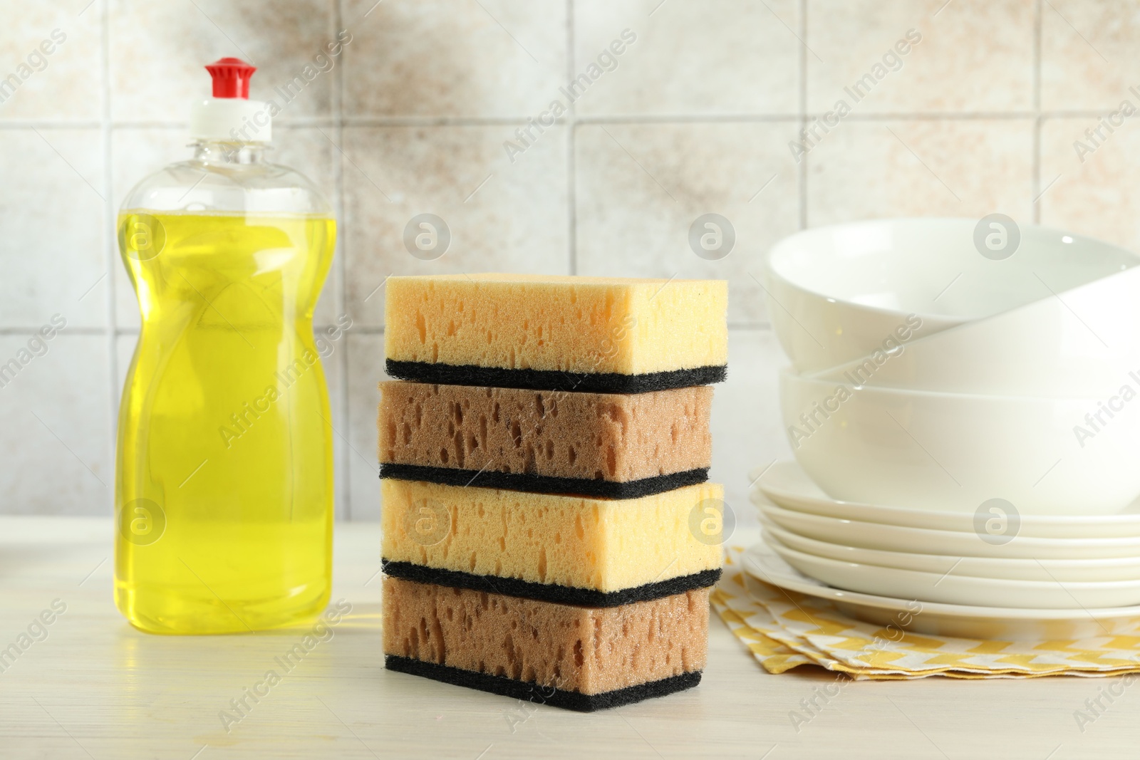 Photo of Stack of sponges, detergent and dishware on light wooden table, closeup