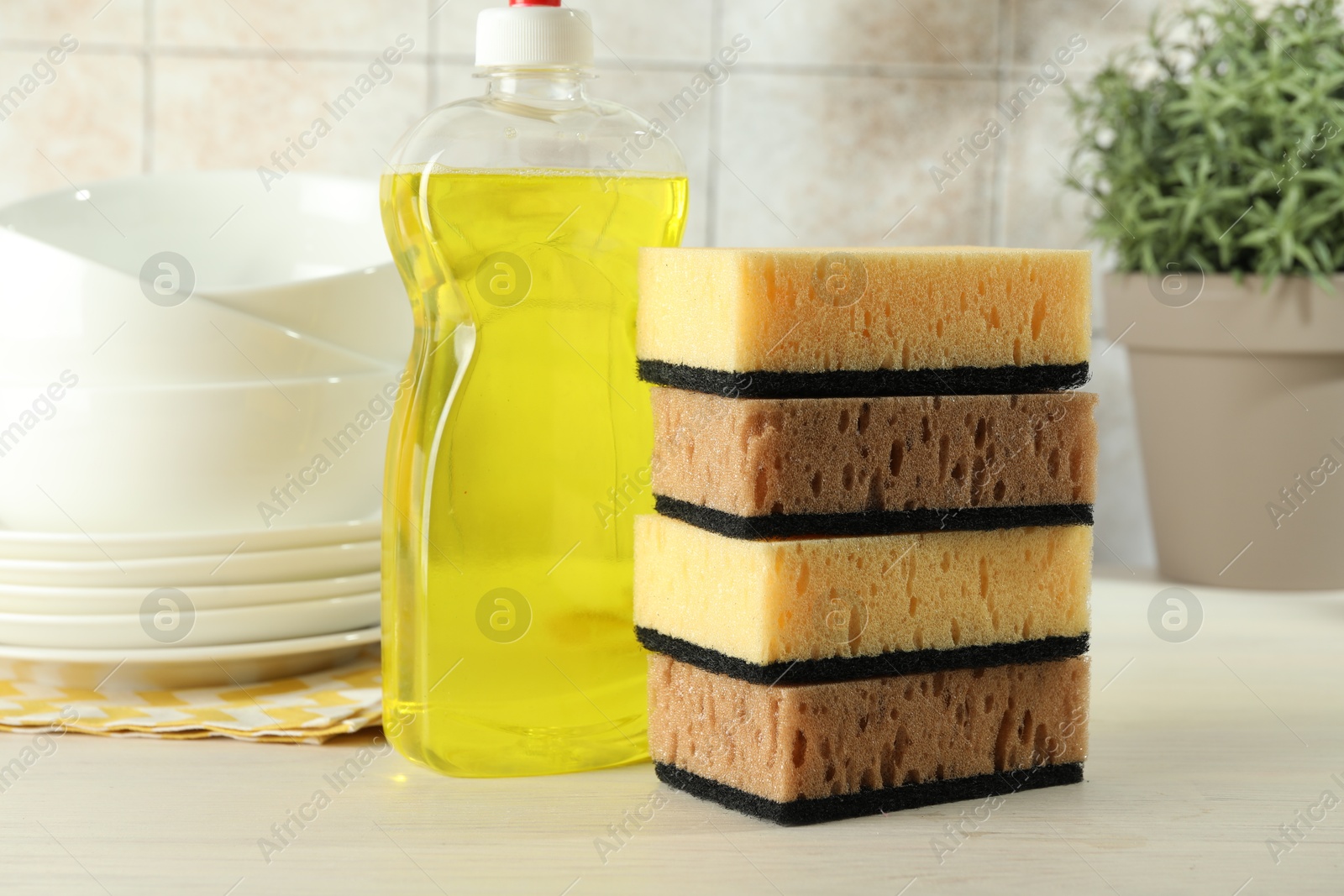 Photo of Stack of sponges, detergent and dishware on light wooden table, closeup