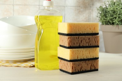 Photo of Stack of sponges, detergent and dishware on light wooden table, closeup