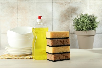 Photo of Stack of sponges, detergent and dishware on light wooden table, closeup