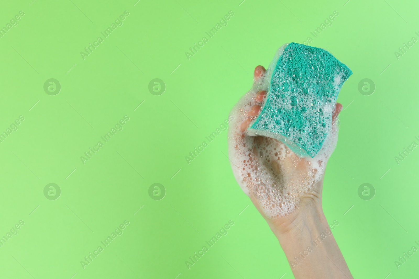 Photo of Woman holding sponge with foam on green background, closeup. Space for text