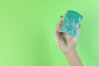 Photo of Woman holding sponge with foam on green background, closeup. Space for text