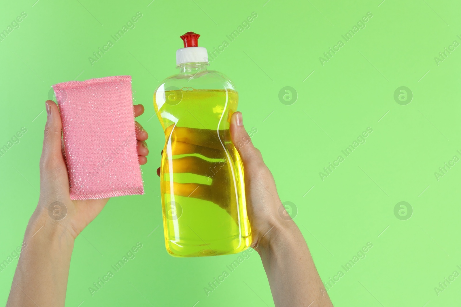 Photo of Woman holding sponge and bottle with detergent on green background, closeup. Space for text