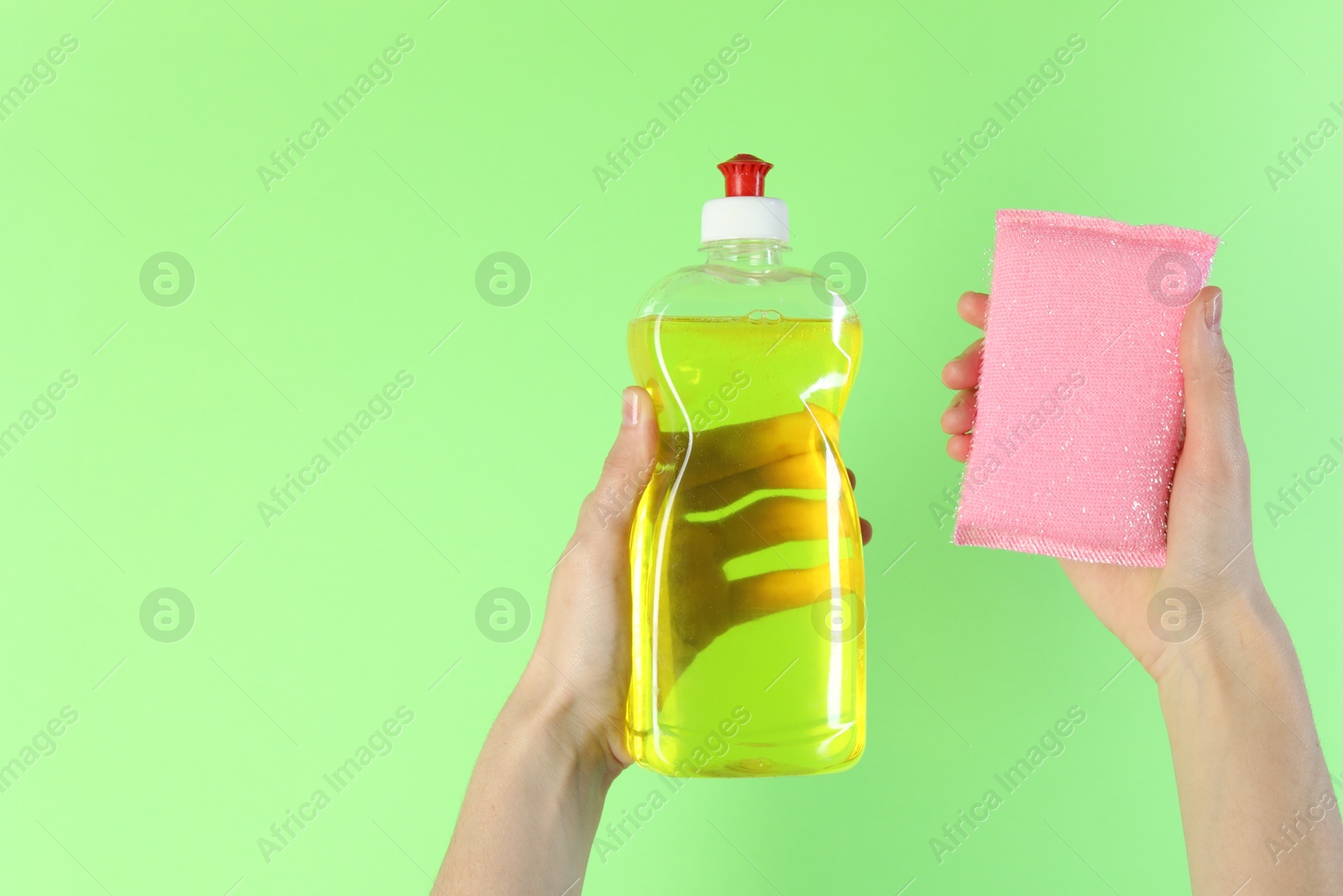 Photo of Woman holding sponge and bottle with detergent on green background, closeup. Space for text