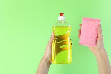 Photo of Woman holding sponge and bottle with detergent on green background, closeup. Space for text