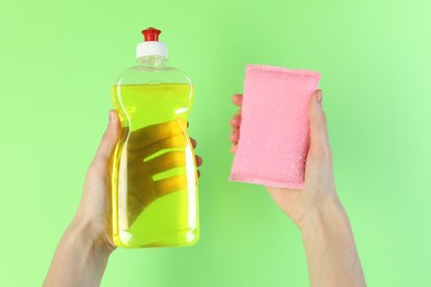 Photo of Woman holding sponge and bottle with detergent on green background, closeup