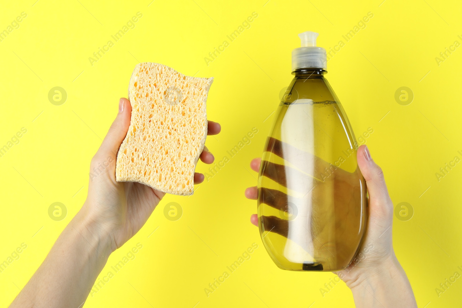 Photo of Woman holding sponge and bottle with detergent on yellow background, closeup