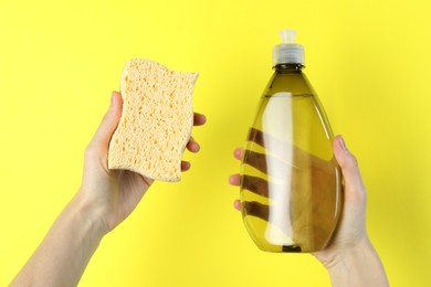 Photo of Woman holding sponge and bottle with detergent on yellow background, closeup